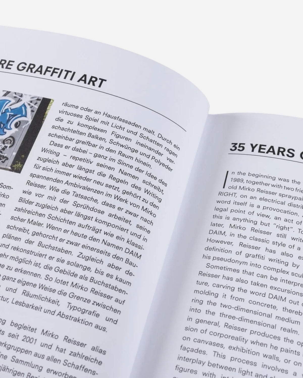Open pages of the Astrofat DAIM Retrospective book featuring text and a graffiti photo in English and German.