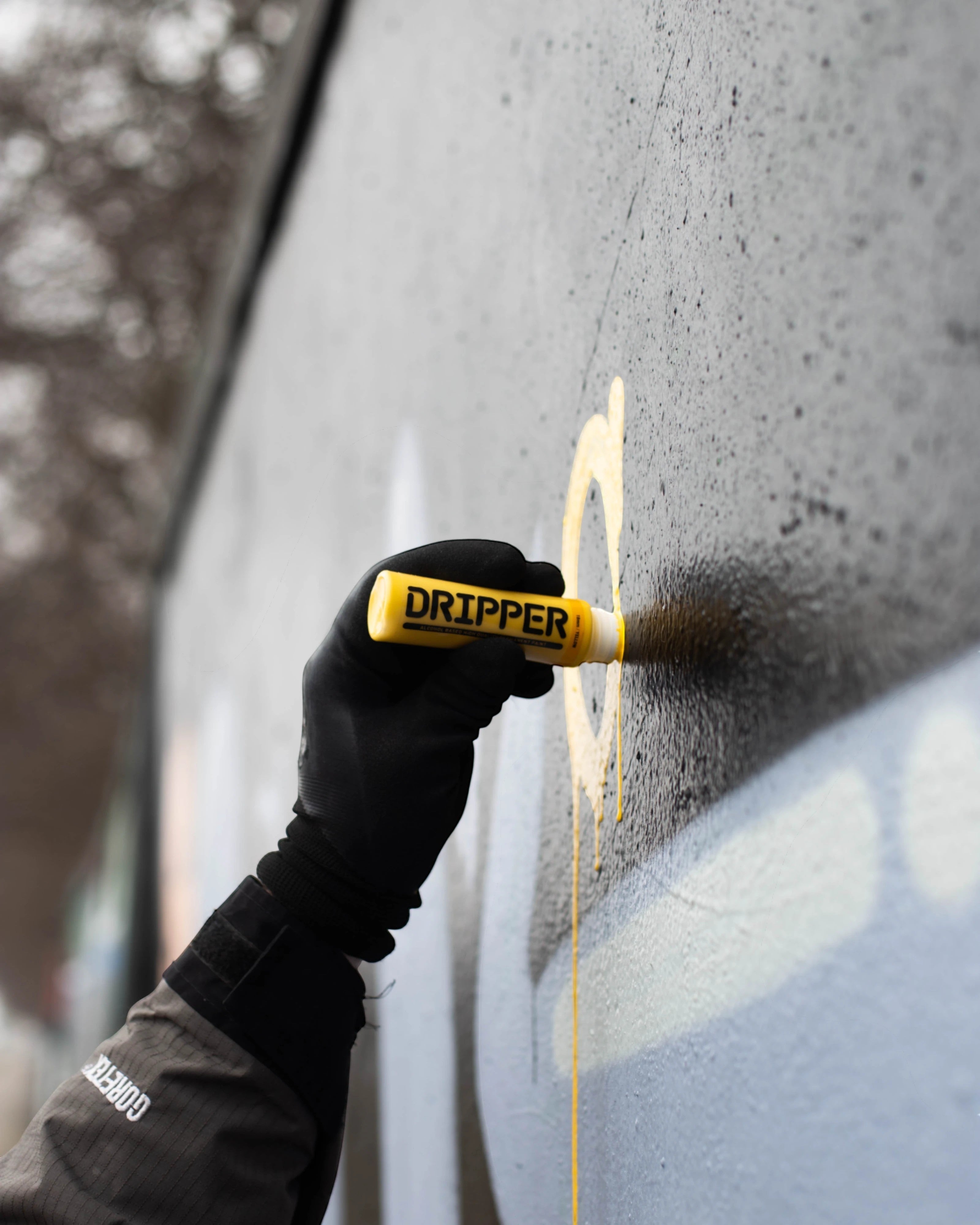 Astrofat Dripper 18mm yellow tagging marker with a black gloved hand writing on a wall.