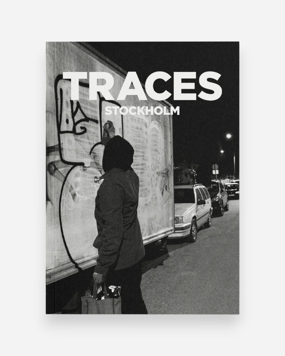 Astrofat Traces Stockholm book cover featuring a person in a hooded jacket spray painting graffiti on a truck at night.